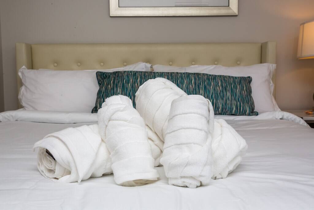 A neatly made bed with white and teal pillows, a beige headboard, and a framed picture on the wall.