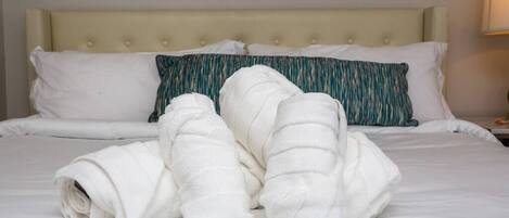 A neatly made bed with white and teal pillows, a beige headboard, and a framed picture on the wall.
