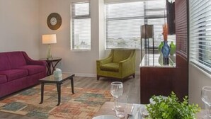 A living room with a purple sofa, a green armchair, and a dining area set with white plates and glasses.