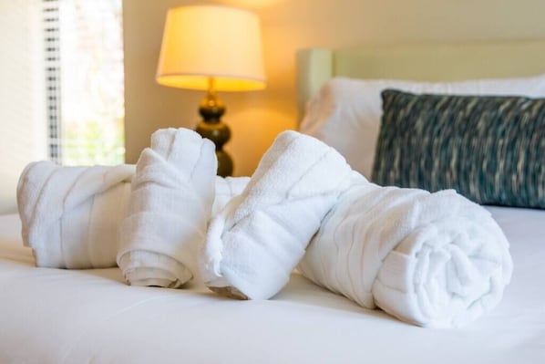A neatly made bed with rolled white towels, a lamp, and a green pillow. - Spacious 500 sqft Studio with Balboa Park View (San Diego)