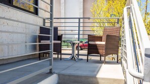 Ein Balkon mit Korbstühlen und einem Tisch, eine Treppe sowie der Blick auf ein rotes Auto und gelbe Bäume.