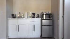 Een kleine keuken met witte kasten, een roestvrijstalen koelkast, een magnetron en een koffiezetapparaat.