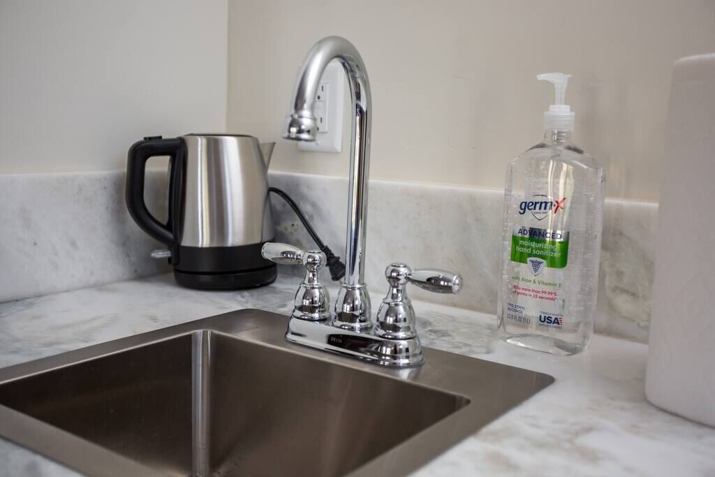 A stainless steel sink with a modern faucet, a black electric kettle, and a bottle of Germ-X hand sanitizer.