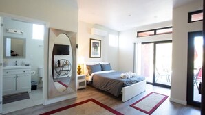 Een moderne slaapkamer met een bed, nachtkastje en een grote spiegel. Er is een schuifdeur van glas die leidt naar een buitengebied.