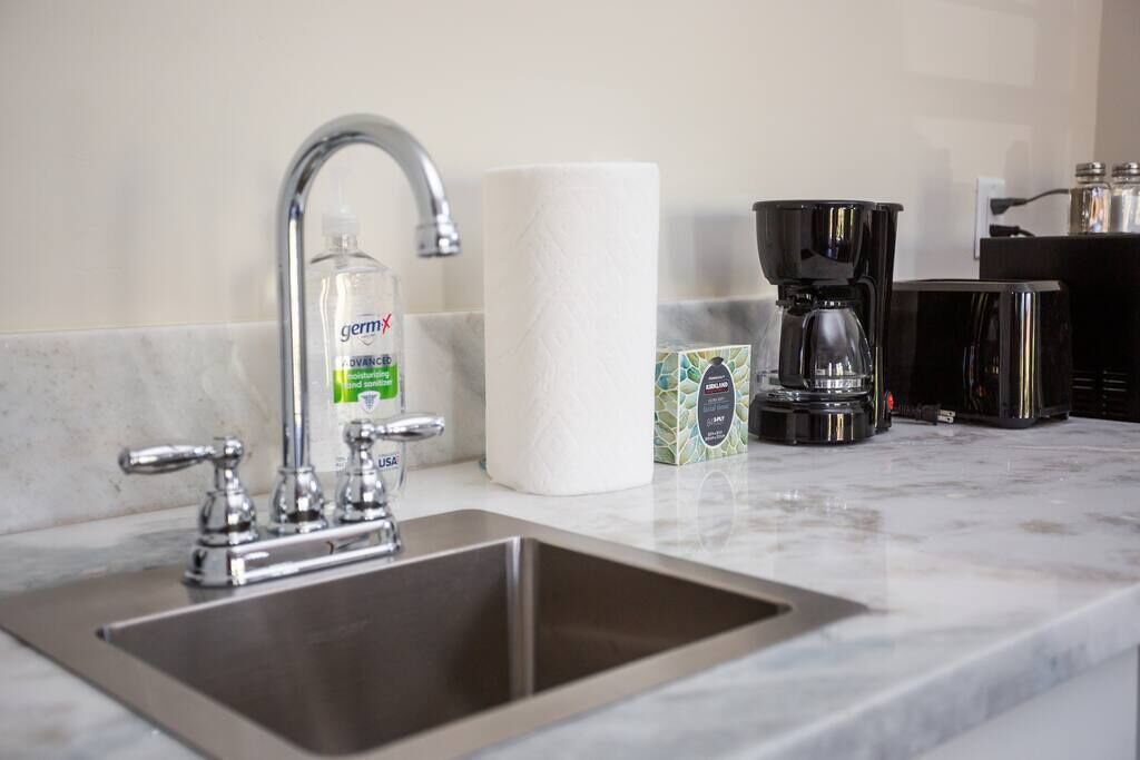 A kitchen with a stainless steel sink, a paper towel dispenser, a coffee maker, and a box of coffee pods.