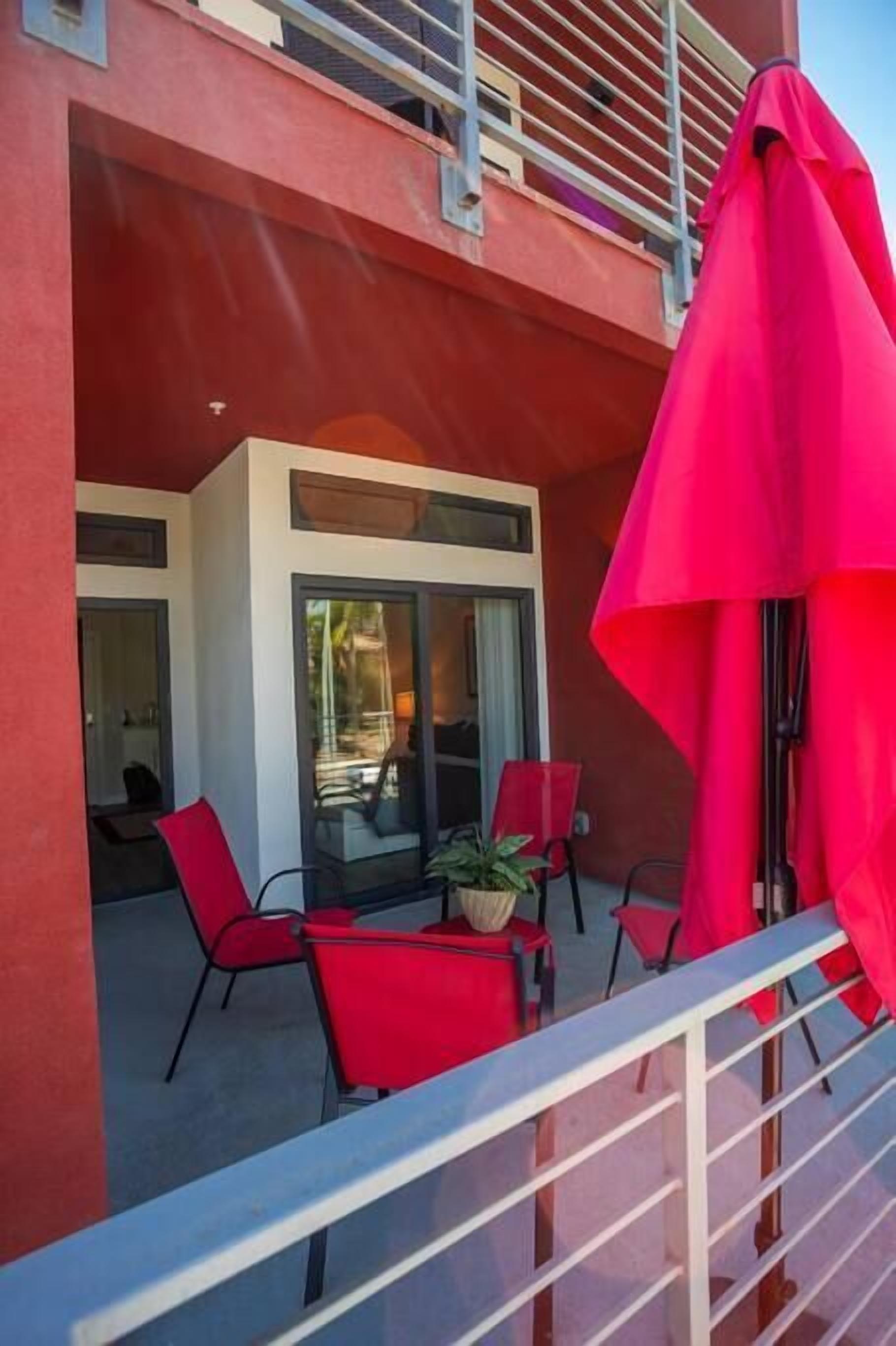 Un área de estar al aire libre moderna con sillas rojas y un paraguas rojo grande.
