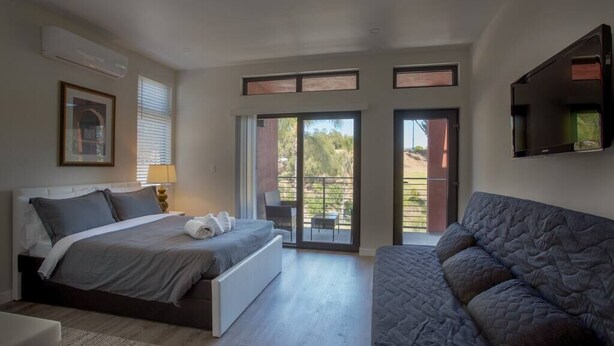 Ein Schlafzimmer mit Bett, einer Couch, einem Fernseher und einem Balkon mit Blick.
