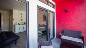 Ein modernes Interieur mit einer roten Akzentwand, einer Glastür zur Schlafkammer, einem schwarzen Sofa und Korbmöbeln.