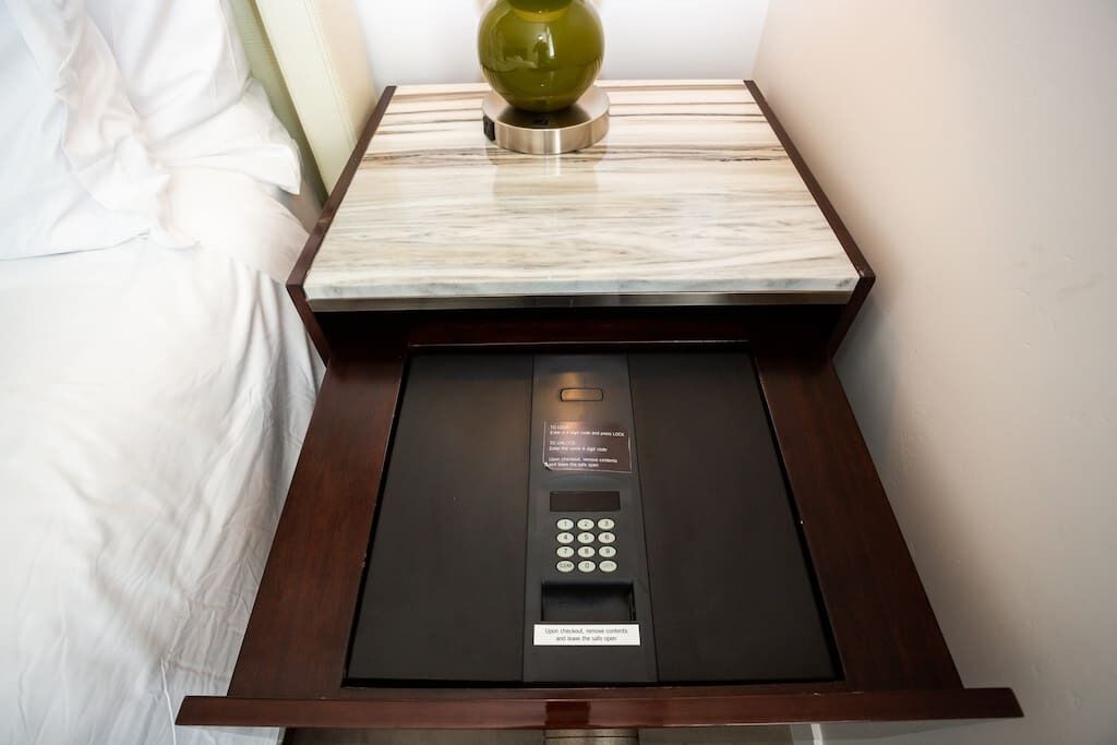 Une chambre d’hôtel dotée d’une table de chevet au plateau en marbre, d’un vase vert et d’un coffre-fort encastré avec un clavier numérique.