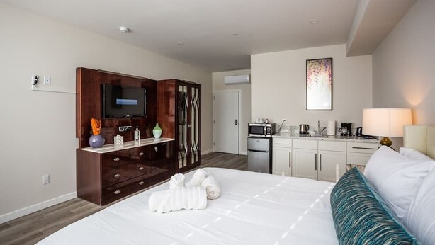 A hotel room with a bed, a TV, a minibar, a desk, and a kitchenette.