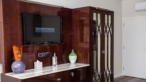 A room with a TV mounted on a wooden cabinet, a marble countertop with decorative items, and a glass-fronted cabinet.