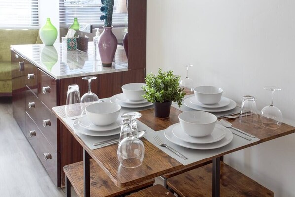 A dining table set with white plates, bowls, and wine glasses, accompanied by a potted plant and decorative vases.