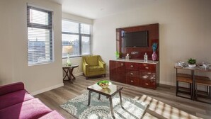 Een woonkamer met een bank, een televisie, een houten kast en een eethoek met een tafel en stoelen.