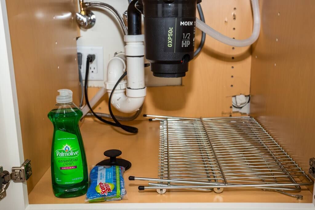 A kitchen with a sink, a dish rack, a dish soap bottle, and a coffee maker.