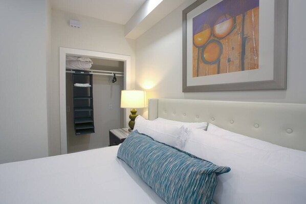 A hotel room with a bed, a nightstand, a lamp, a closet, and a painting on the wall.