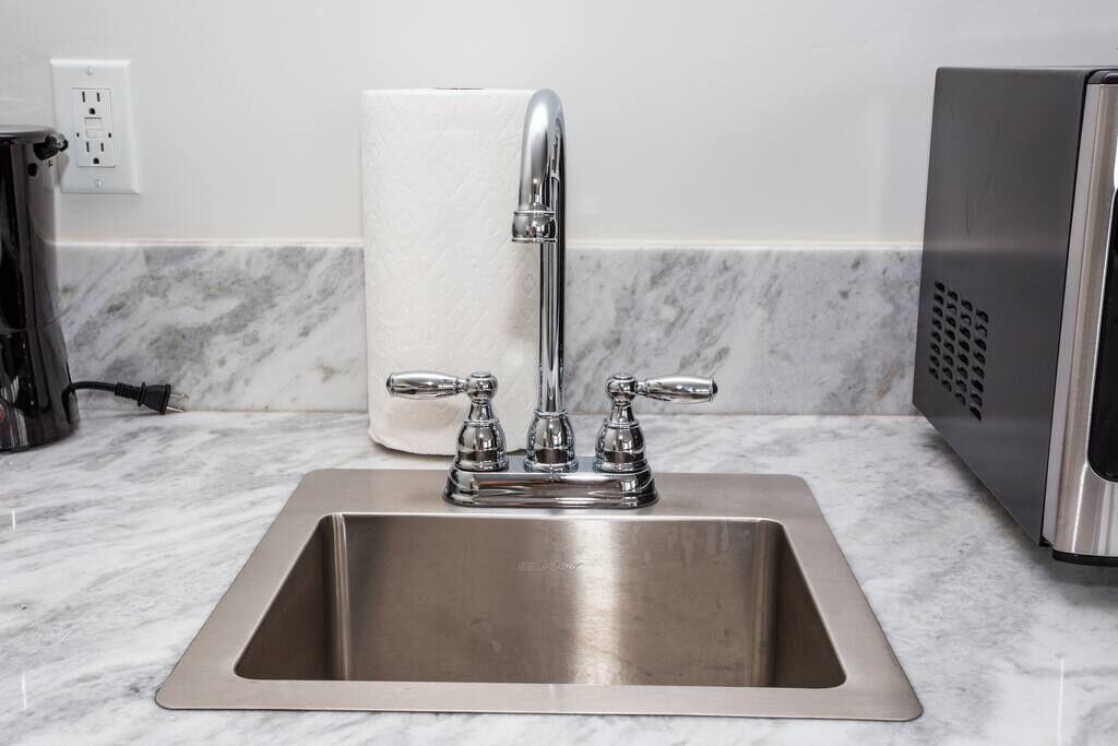 A stainless steel kitchen sink with a single faucet and a paper towel dispenser.