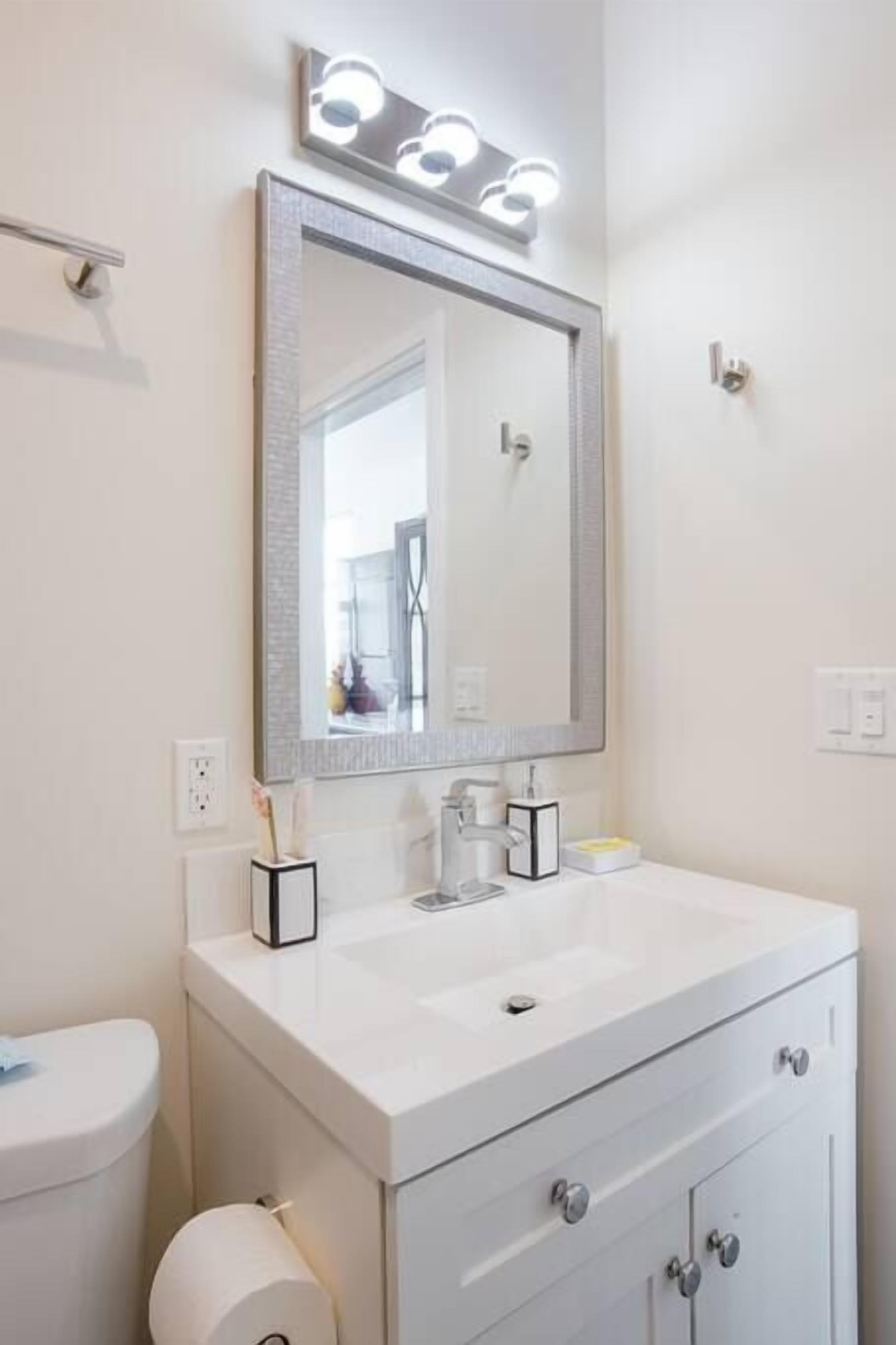 Une salle de bain avec un lavabo blanc, un grand miroir avec éclairage, des toilettes et un rouleau de papier toilette.