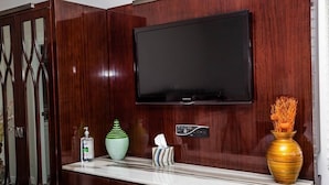 Ein Zimmer mit einem Holzkabinett, einem an der Wand befestigten Flachbildfernseher, einer Marmorplatte, einem grünen Strauß, einem gestreiften Behälter, einem gelben Strauß und einer Handdesinfektionsmittel-Flasche.