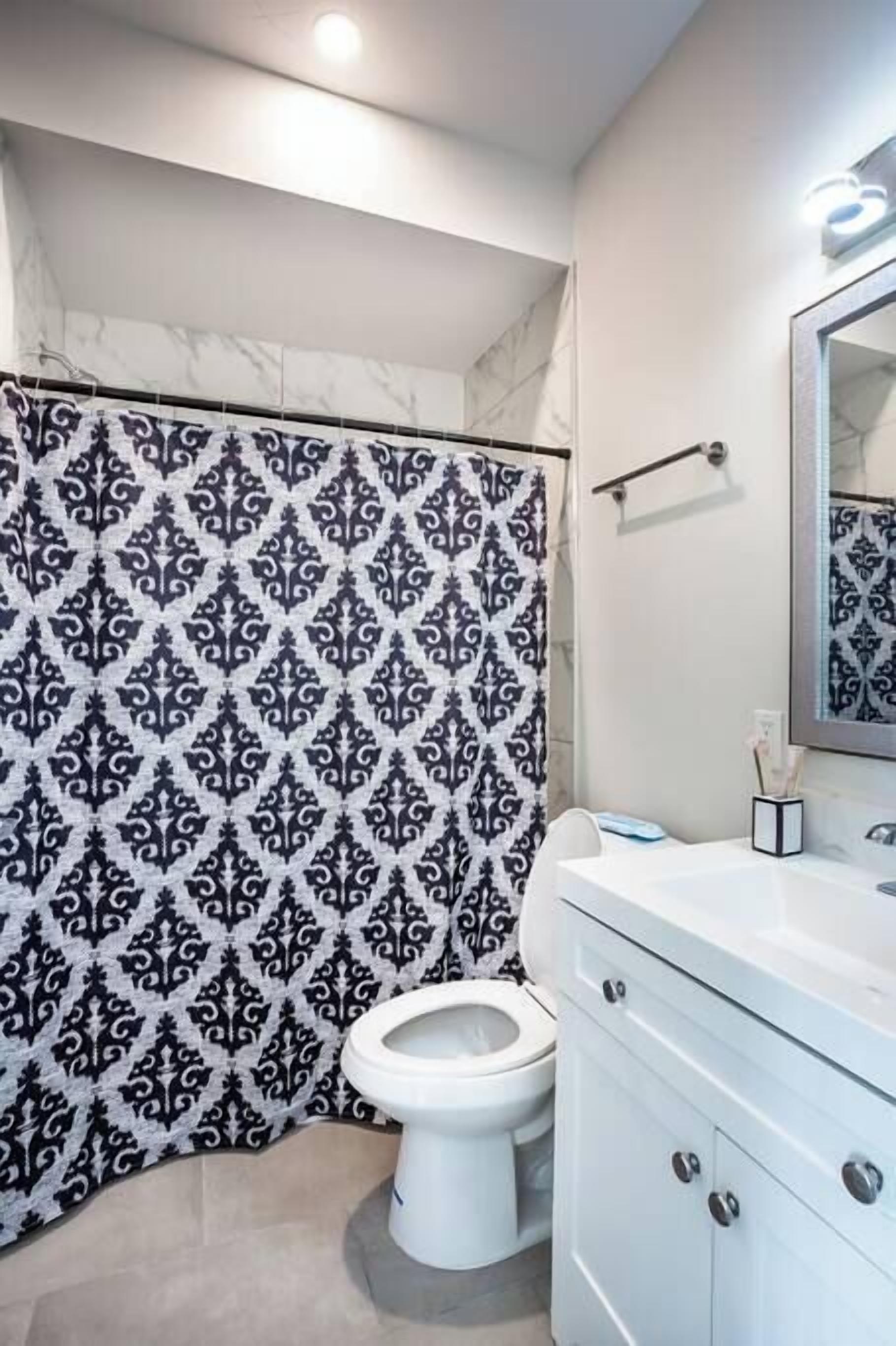 Une salle de bain avec un rideau de douche à motifs, des toilettes blanches et un meuble-lavabo blanc doté de placards.