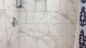 Eine Dusche mit Glastrennwand, Marmorfliesen und Duschkopf.