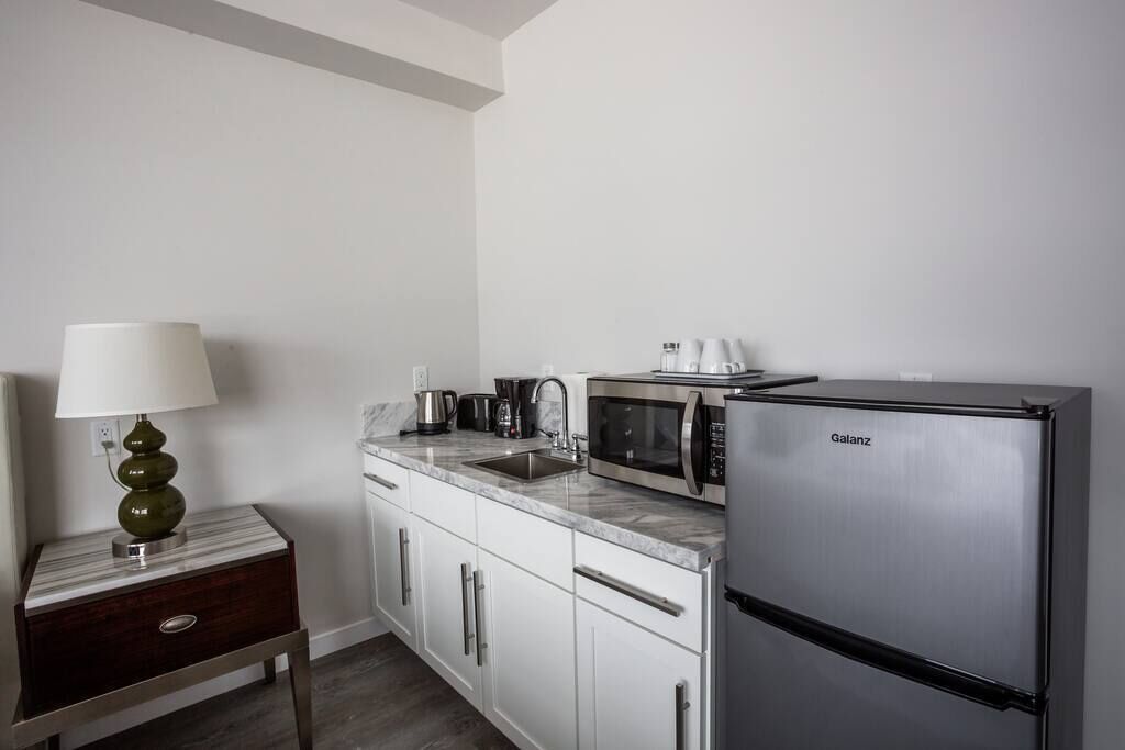 A compact kitchen with white cabinets, a marble countertop, a Galanz refrigerator, a coffee maker, and a lamp.