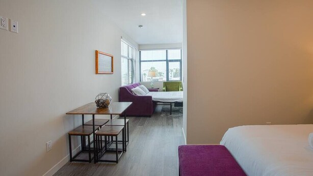 Une chambre d’hôtel moderne équipée d’un lit, d’un petit bureau et d’un coin salon avec un canapé et des fauteuils.