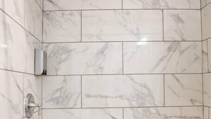 Un espace douche avec des carreaux de marbre blanc et une pomme de douche à main.