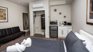 Et moderne hotelværelse med en seng, en sort sofa, et tekøkken og et walk-in closet.