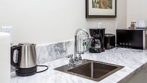 Una cucina moderna con lavandino in acciaio inossidabile, bollitore, macchina da caffè e un quadro astratto appeso al muro.