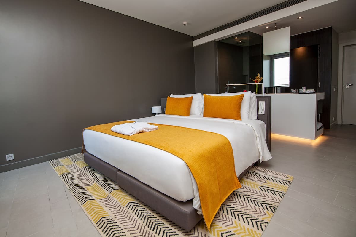 A modern hotel room with a large bed, a bedside table, a built-in desk, and a mirror.