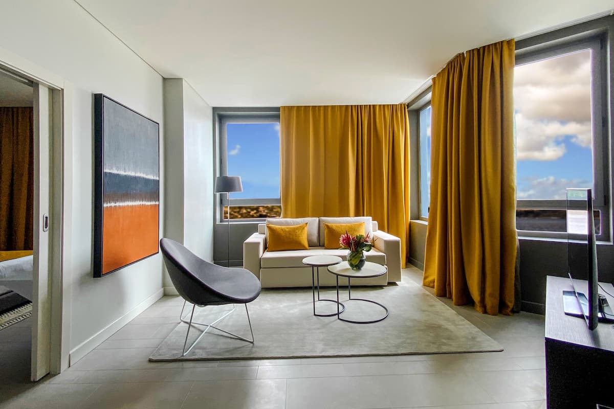 A modern living room with a sofa, a chair, a coffee table, and a large window with curtains.