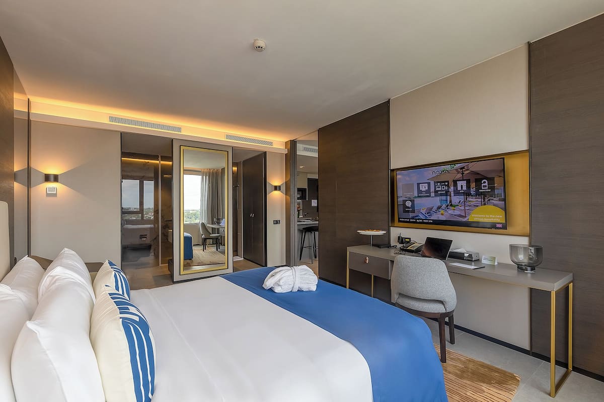 A hotel room with a bed, desk, chair, and a television displaying a welcome message.