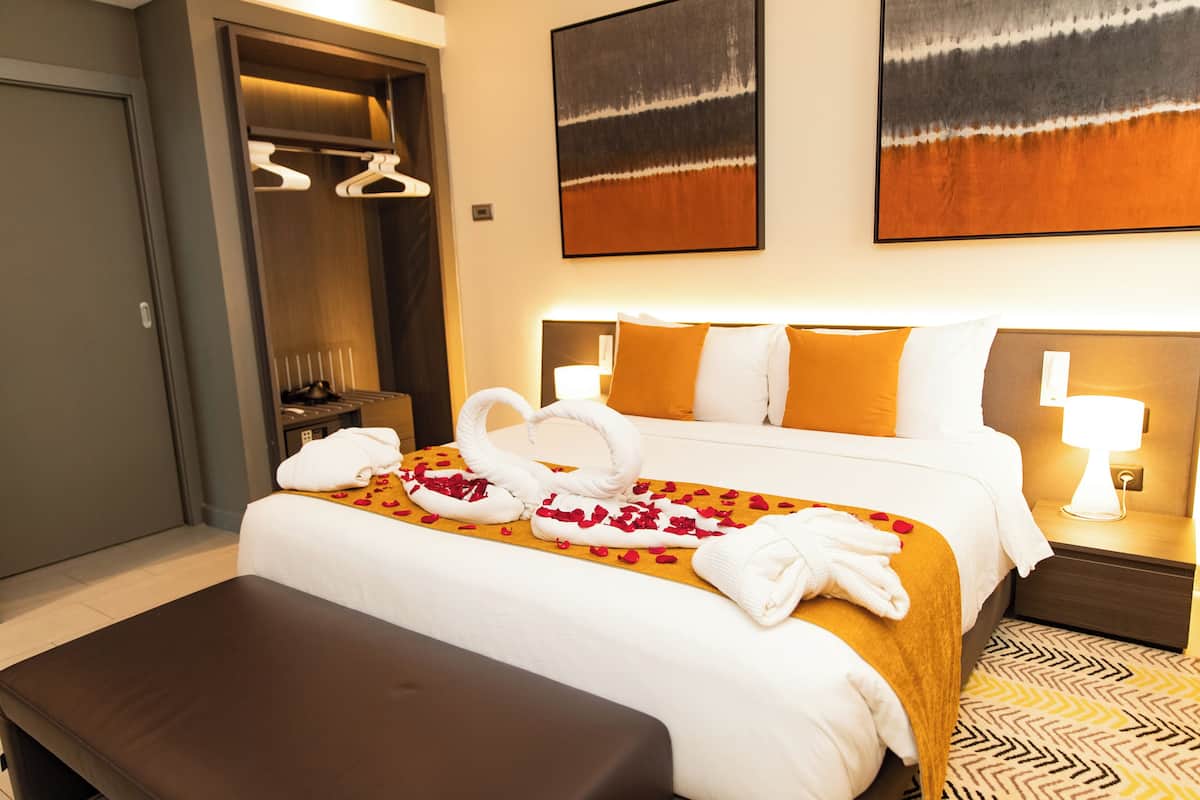 A hotel room with a bed, a bench, a wardrobe, and two wall-mounted lamps.