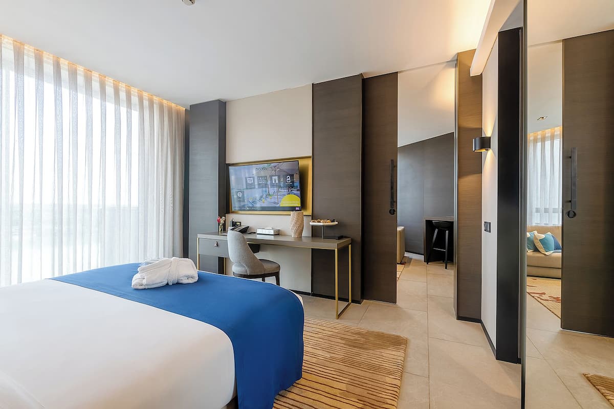 A modern hotel room with a large bed, a desk, a TV, and a sofa.