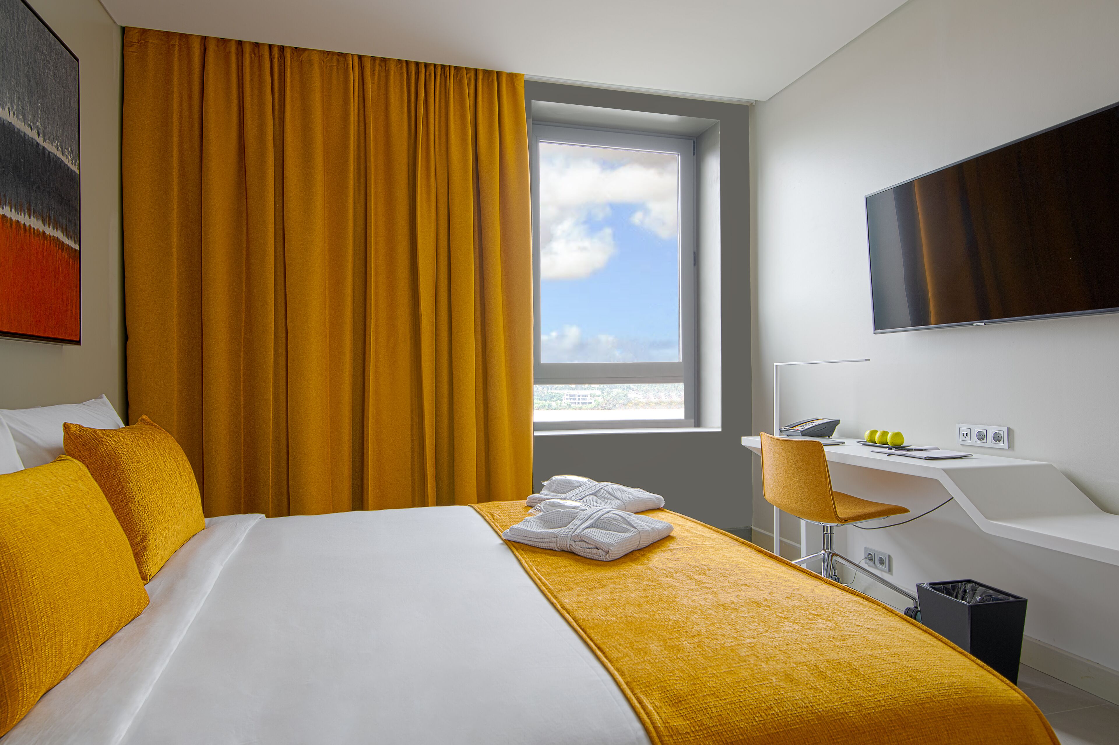 A hotel room with a bed, a desk, a chair, a TV, and a window with a view.