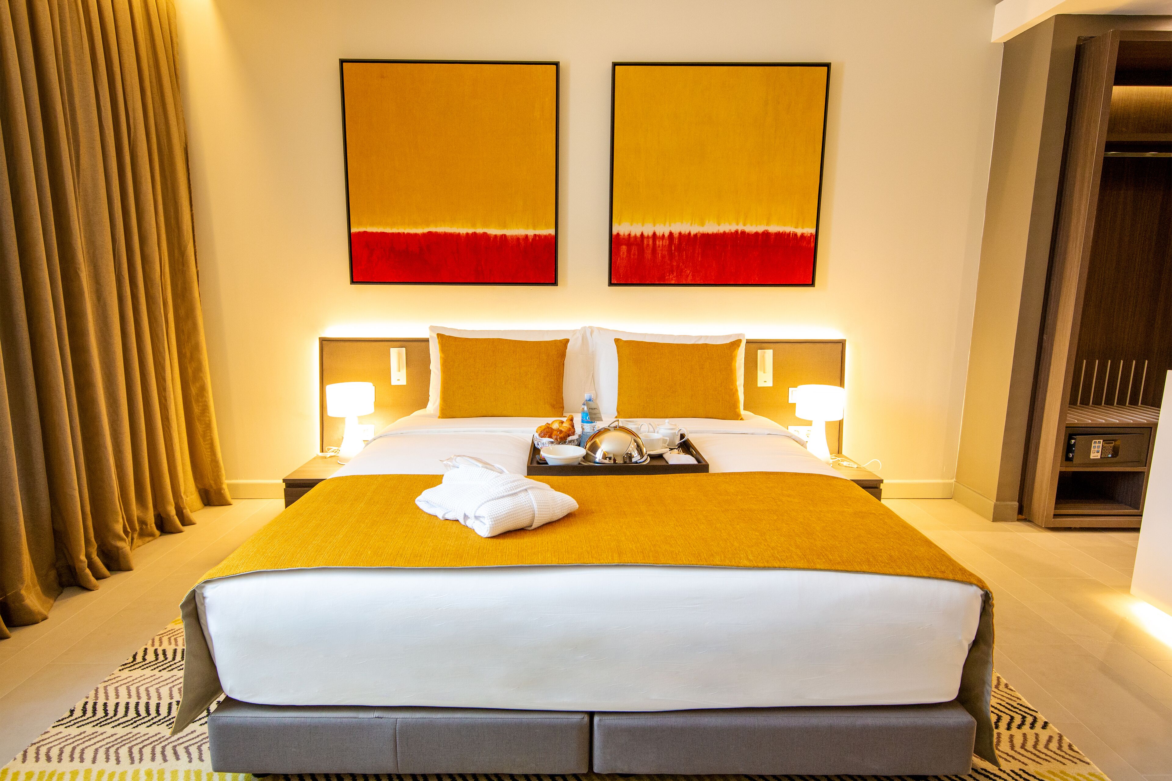 A hotel room with a large bed, two bedside tables, a nightstand, and a wardrobe.