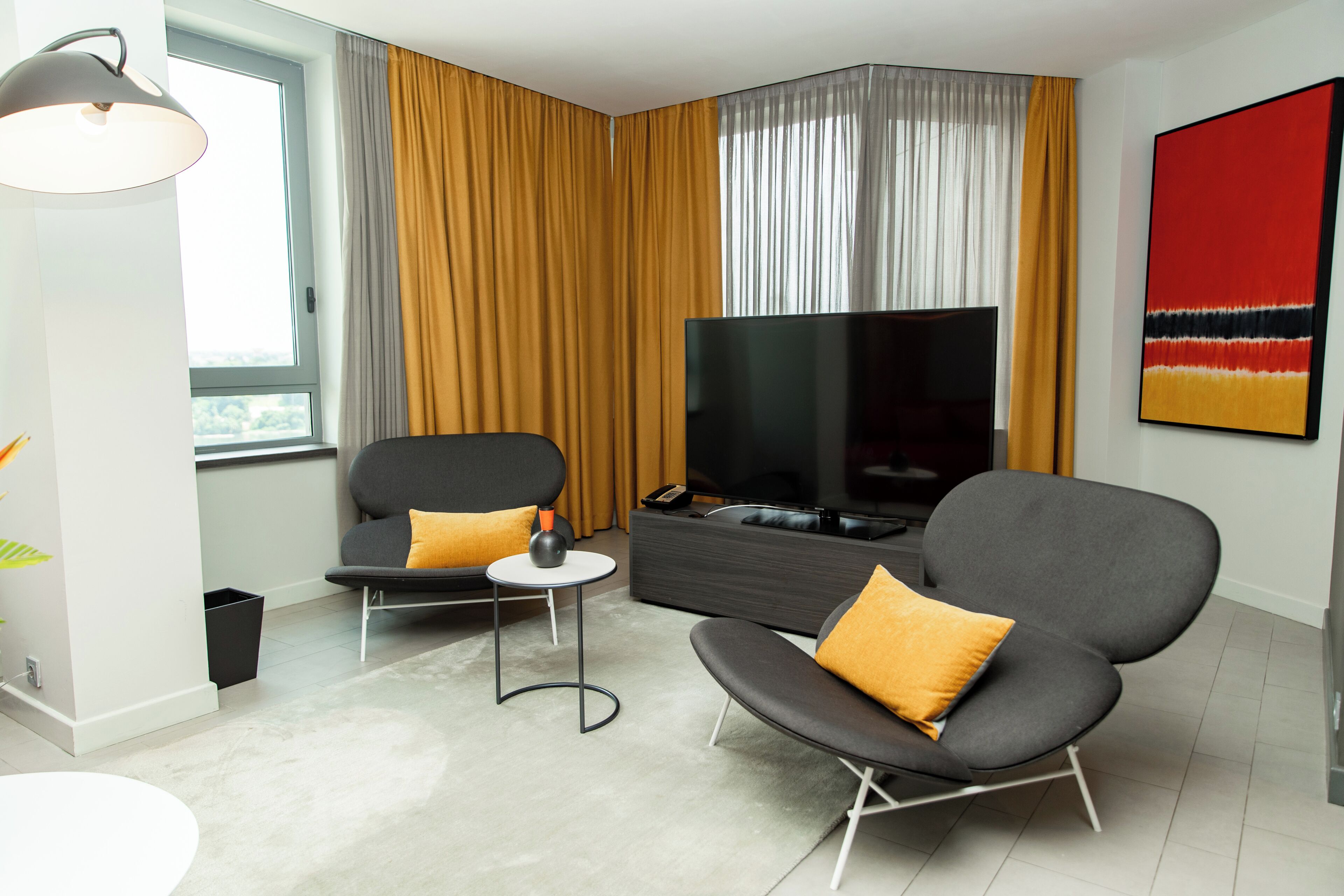 Een moderne woonkamer met een bank, fauteuil, televisie en een schilderij aan de muur.