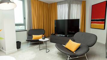Een moderne woonkamer met een bank, fauteuil, televisie en een schilderij aan de muur.