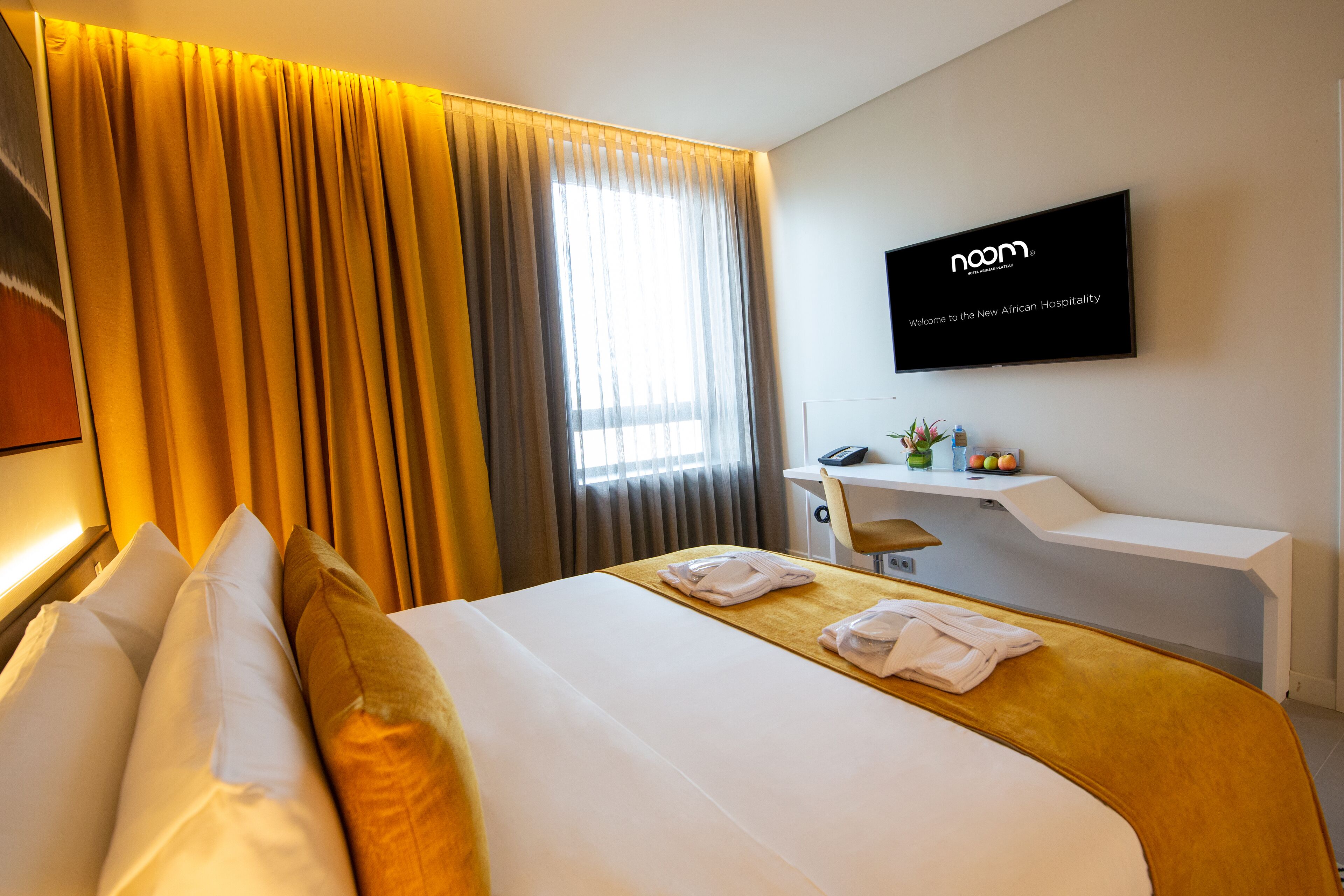 A hotel room with a bed, a desk, a TV, and a window with curtains.