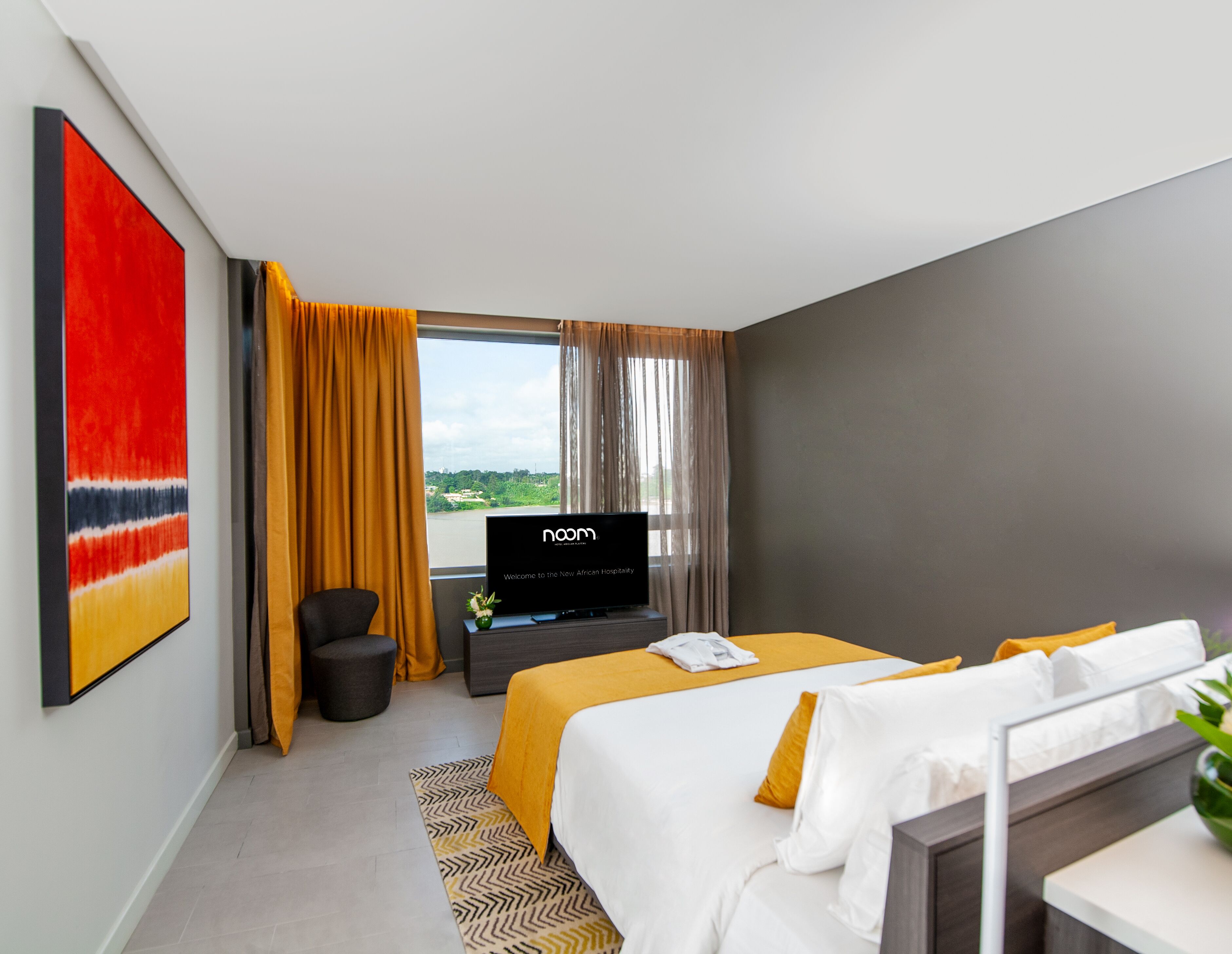 A hotel room with a bed, a TV, a desk, and a window with curtains.