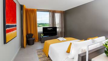 A hotel room with a bed, a TV, a desk, and a window with curtains.