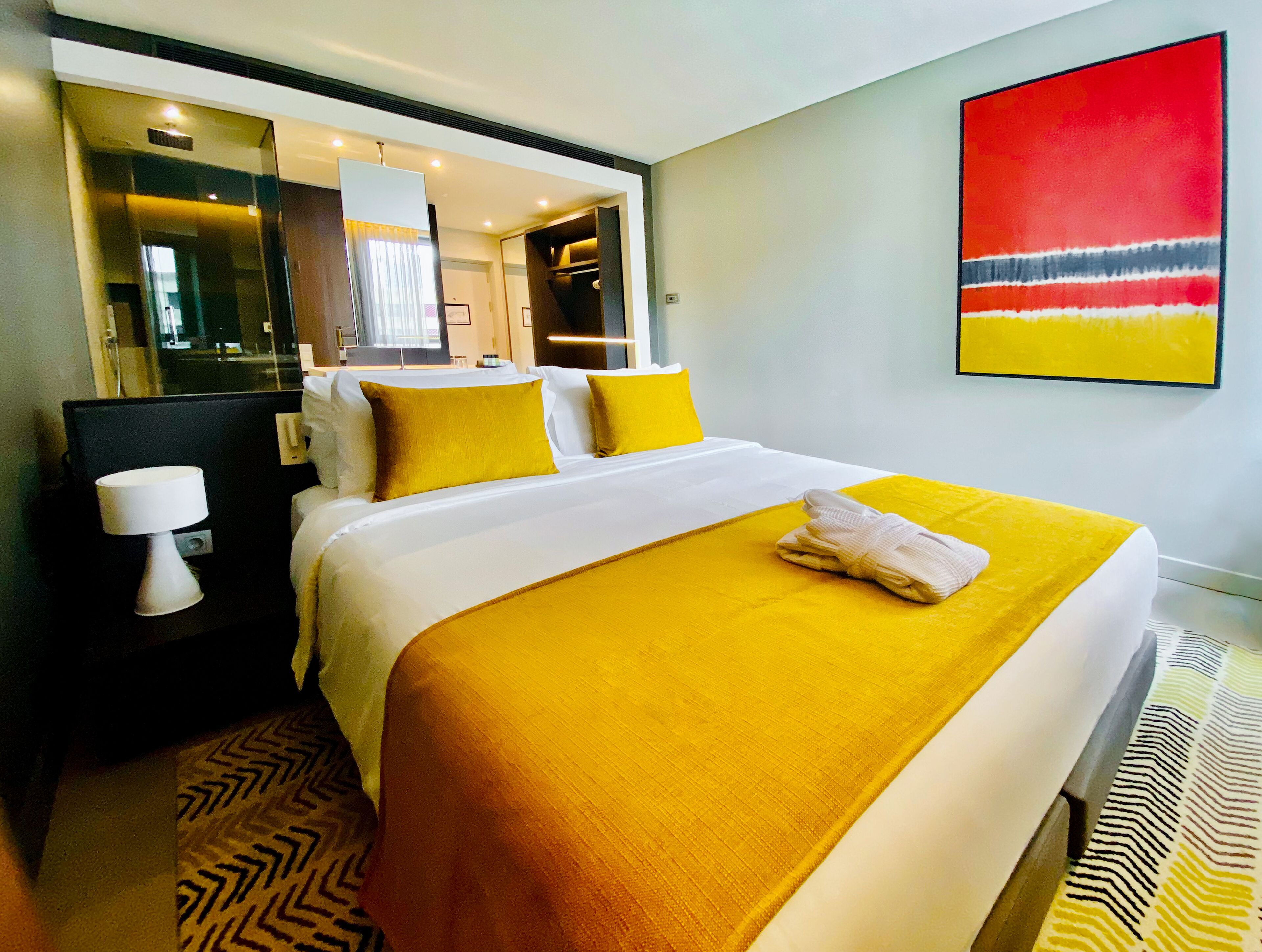 A hotel room with a large bed, a nightstand, a mirror, and a red abstract painting on the wall.