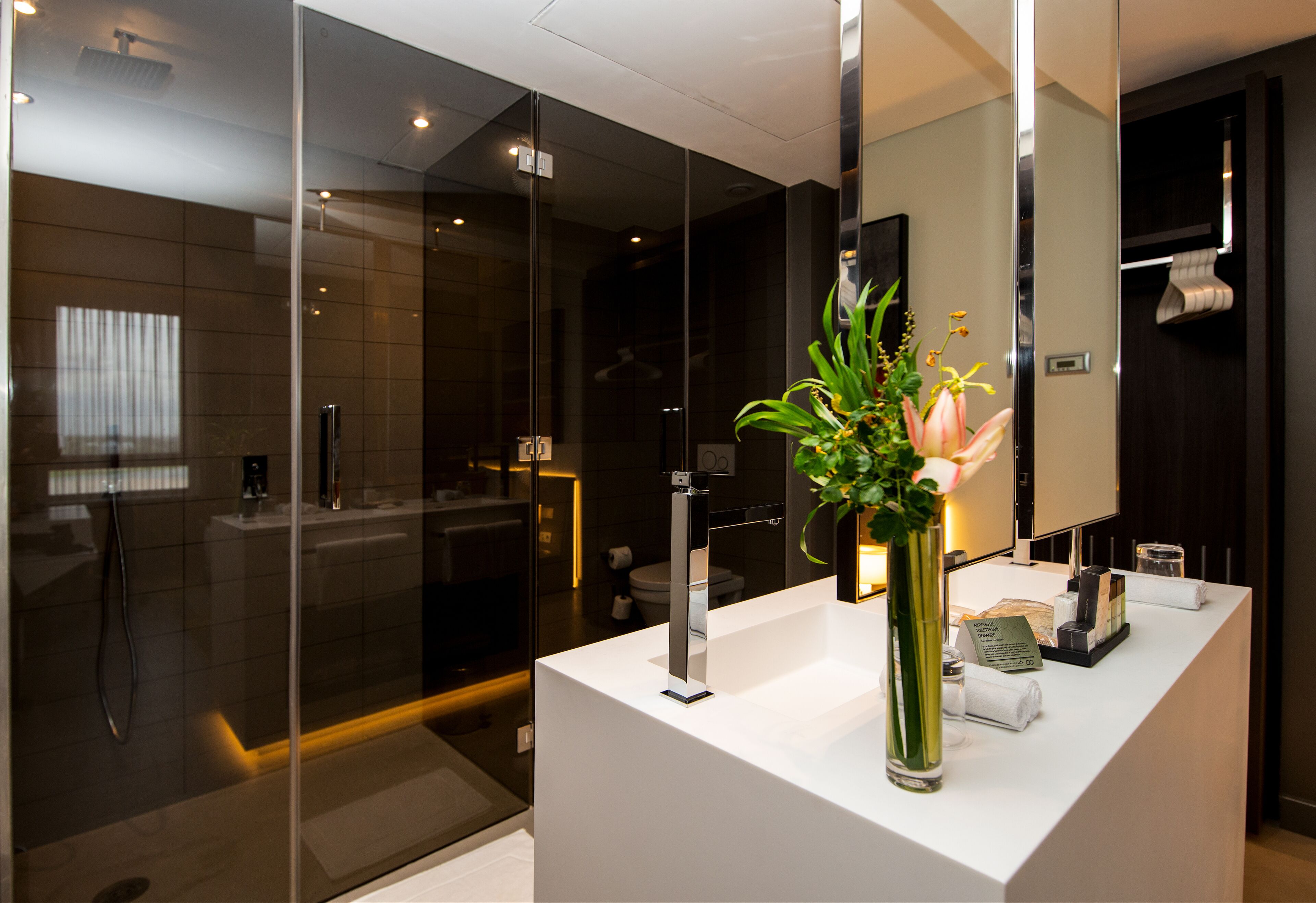 A modern bathroom with a glass-enclosed shower, a white vanity with a mirror, and a vase with flowers.