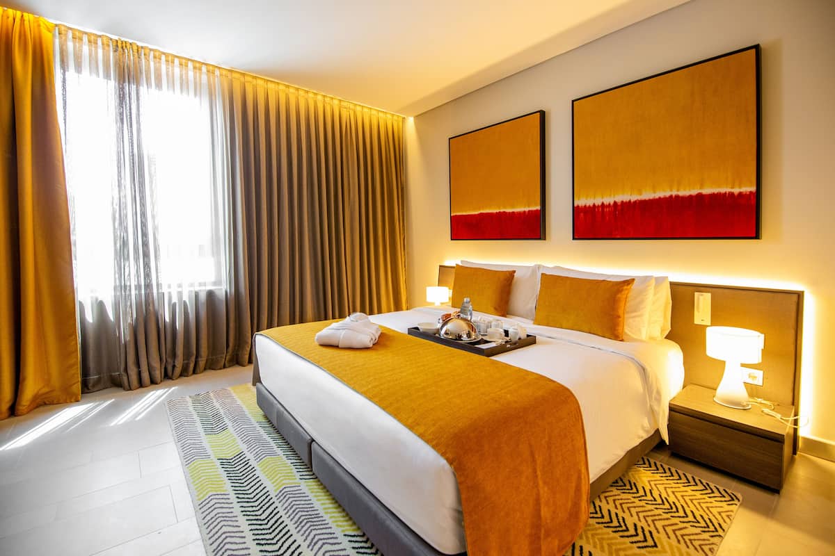 A hotel room with a large bed, a nightstand with a lamp, and two wall-mounted artworks.