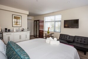 A hotel room with a bed, a sofa, a TV, a desk with a chair, a window with blinds, and a kitchen area. - Next to San Diego Downtown - Cali King Size Studio (San Diego)