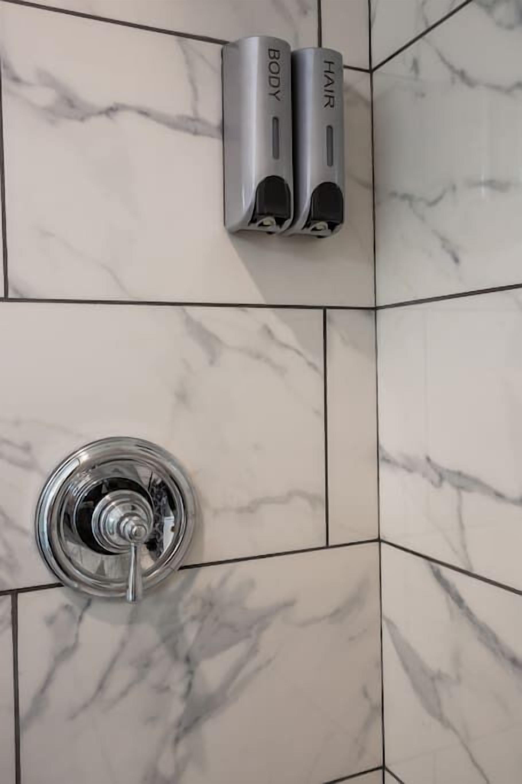 A bathroom with marble tiles, a hand dryer, and a showerhead.