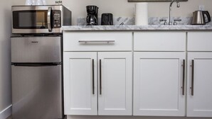 Eine Küche mit einem Edelstahl-Kühlschrank, einer Mikrowelle, einer Kaffeemaschine und einem Waschbecken mit Armatur.