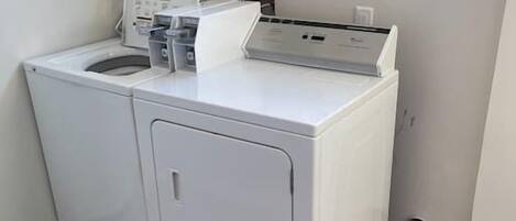 A compact laundry room with a front-loading washer and dryer, a small window, and a wooden floor.