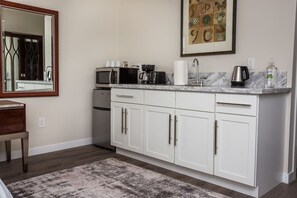 A modern kitchen with white cabinets, a marble countertop, a coffee maker, a kettle, and a framed artwork above the sink.