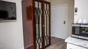 Een kamer met een houten garderobe, een aan de muur bevestigde televisie, een magnetron op een marmeren aanrechtblad en een witte deur.